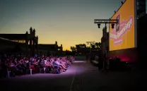 Gente mira a una pantalla gigante al aire libre al atardecer