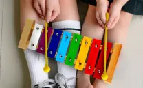 Las piernas de una niña y un niño sujetan un xilófono de colores