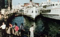 Gente observa un barco atracado en un puerto